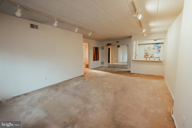 spare room featuring rail lighting, concrete floors, and visible vents