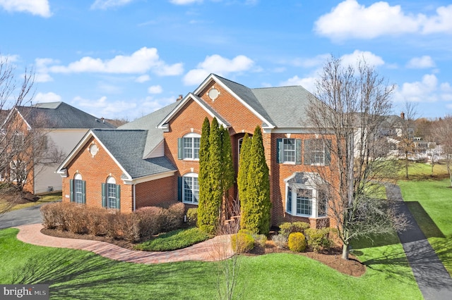 view of front of property with a shingled roof, a front yard, a chimney, and brick siding