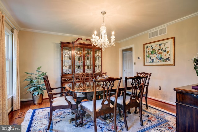 dining area with wood finished floors, visible vents, baseboards, ornamental molding, and an inviting chandelier