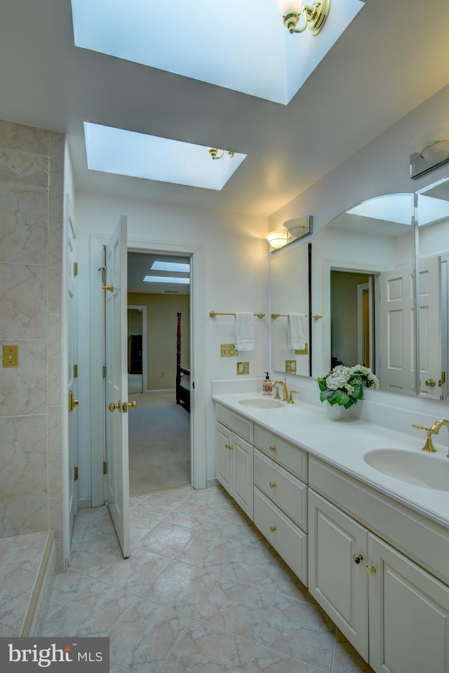 full bathroom featuring a skylight, marble finish floor, a sink, and double vanity