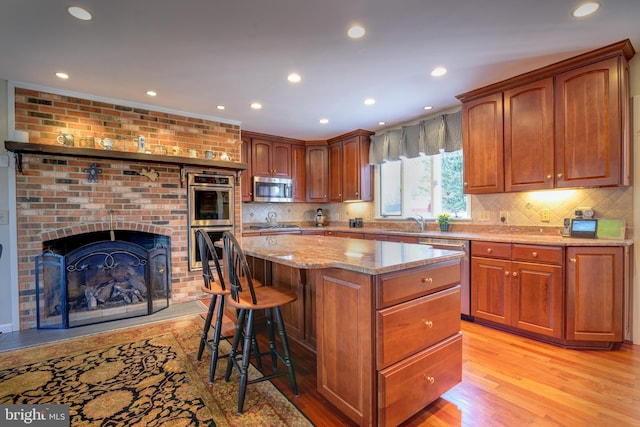 kitchen with light wood-style flooring, a center island, light stone countertops, stainless steel appliances, and a sink