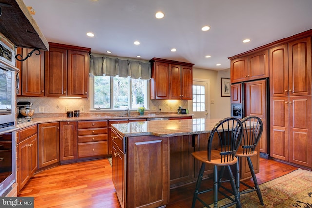 kitchen featuring a kitchen island, a sink, light stone countertops, light wood-type flooring, and oven