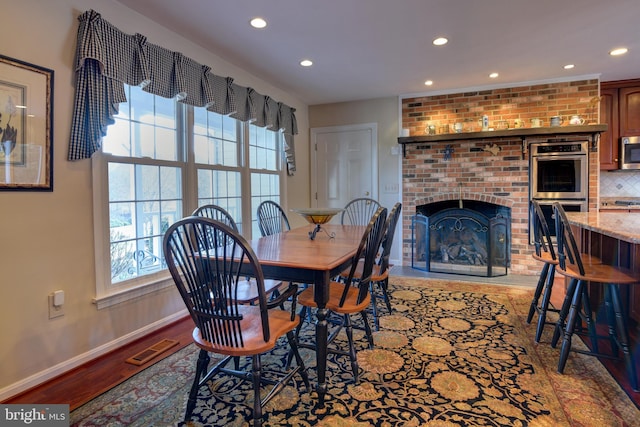 dining room featuring baseboards, visible vents, wood finished floors, a brick fireplace, and recessed lighting