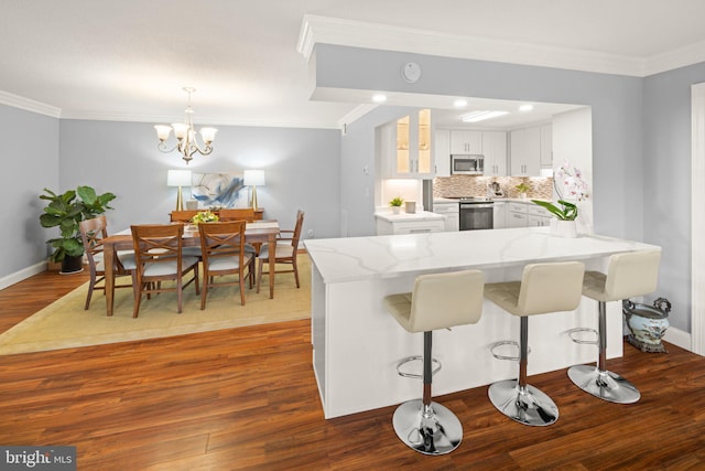 kitchen featuring dark wood-style floors, stainless steel appliances, ornamental molding, light stone countertops, and a peninsula