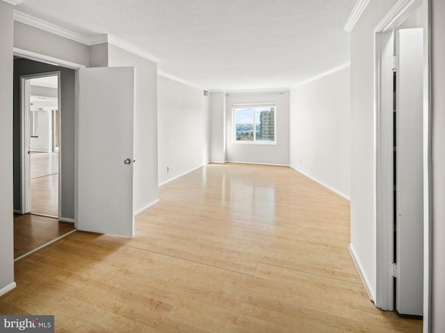 empty room featuring light wood finished floors, a textured ceiling, baseboards, and crown molding