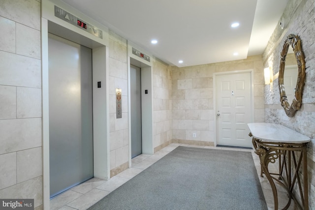 hall featuring elevator, light tile patterned flooring, and tile walls