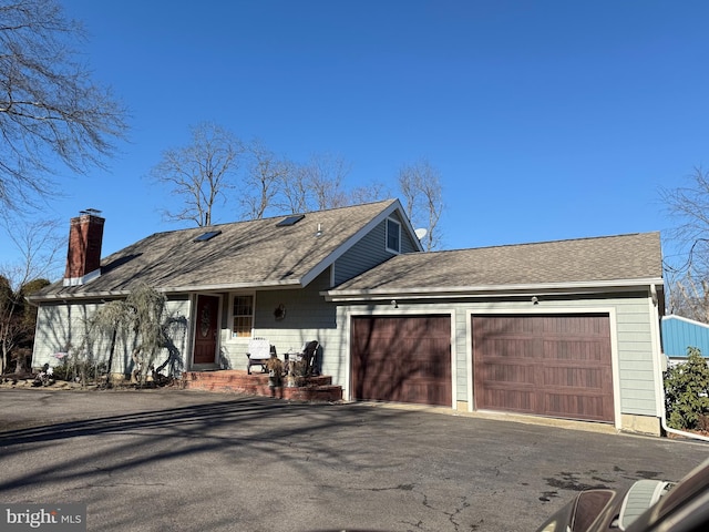 view of front facade with driveway, a chimney, an attached garage, and roof with shingles