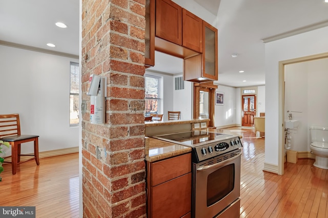 kitchen with ornamental molding, stainless steel electric range, light wood-type flooring, and light stone countertops