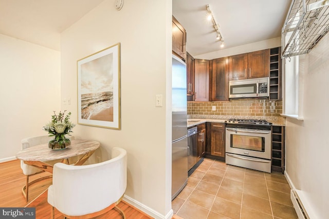 kitchen with backsplash, baseboards, light stone counters, baseboard heating, and stainless steel appliances