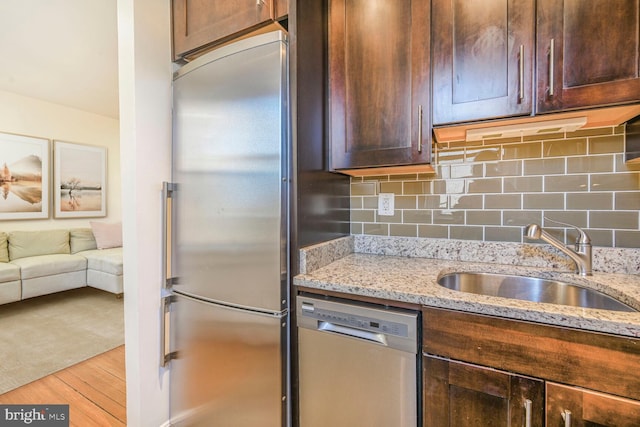 kitchen featuring light stone countertops, wood finished floors, a sink, dark brown cabinetry, and appliances with stainless steel finishes