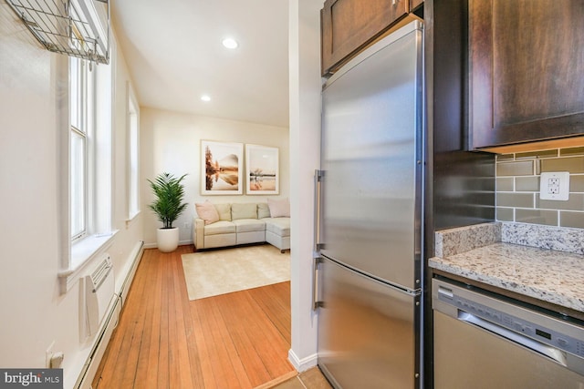 kitchen featuring light stone counters, dark brown cabinetry, light wood-style floors, appliances with stainless steel finishes, and backsplash