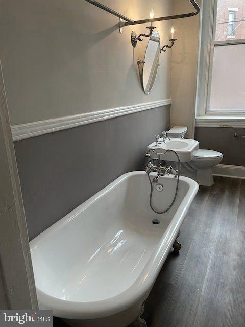 bathroom with hardwood / wood-style floors, a bath, sink, and toilet