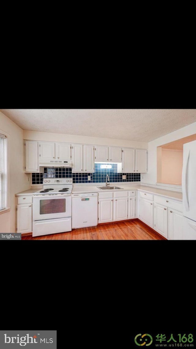 kitchen with light countertops, backsplash, white cabinets, a sink, and white appliances