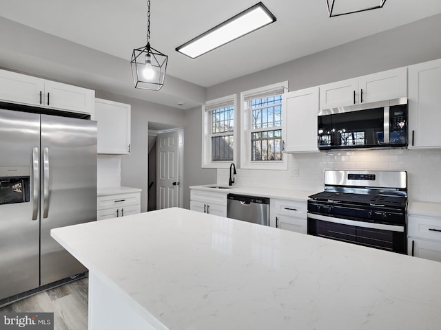 kitchen with hanging light fixtures, stainless steel appliances, tasteful backsplash, light stone countertops, and white cabinets