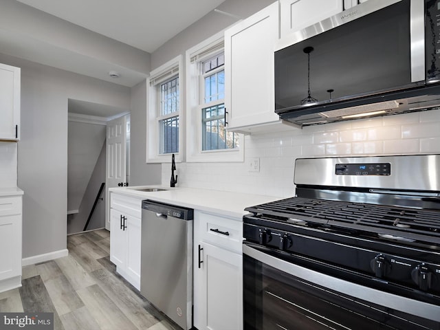 kitchen featuring appliances with stainless steel finishes, tasteful backsplash, sink, white cabinets, and light hardwood / wood-style floors