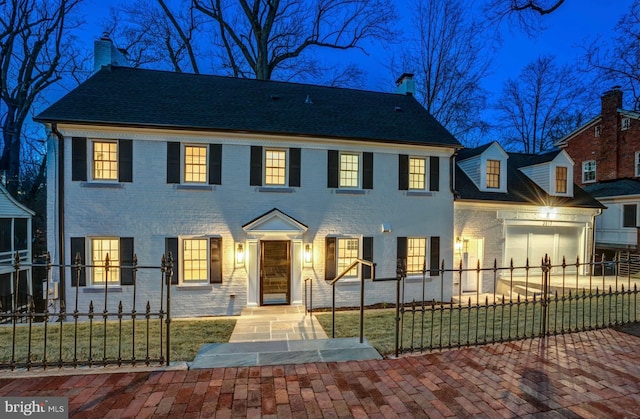 colonial house featuring a garage, a fenced front yard, a chimney, and brick siding