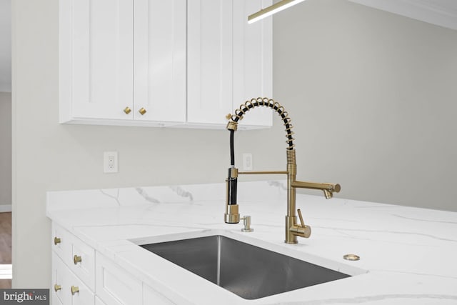 details featuring a sink, light stone countertops, and white cabinets