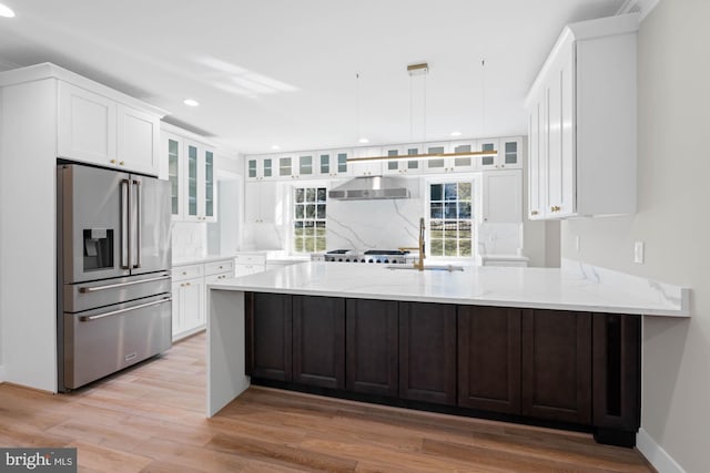 kitchen featuring high end refrigerator, white cabinets, a peninsula, under cabinet range hood, and a sink