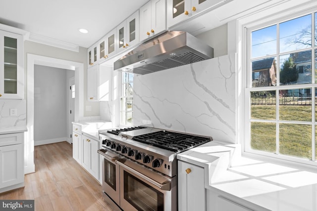 kitchen featuring range with two ovens, light stone countertops, under cabinet range hood, white cabinetry, and decorative backsplash