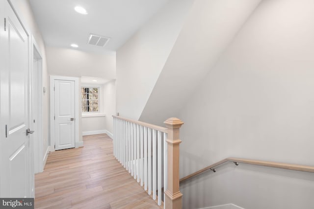 hallway with baseboards, visible vents, wood finished floors, an upstairs landing, and recessed lighting