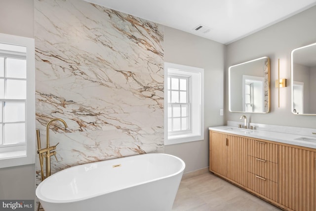 bathroom with double vanity, a soaking tub, visible vents, and a sink