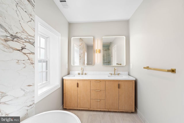 bathroom with double vanity, a soaking tub, visible vents, and a sink