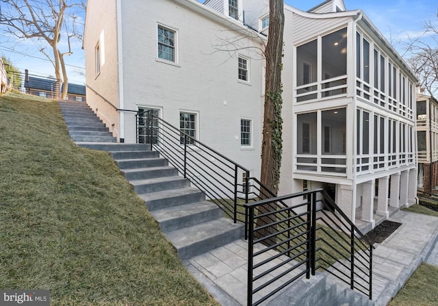 back of house with stairs, brick siding, a lawn, and a sunroom