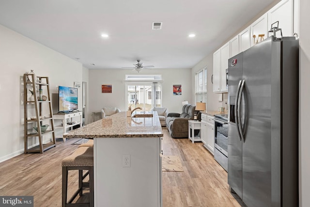 kitchen featuring a center island with sink, stainless steel appliances, white cabinetry, and a breakfast bar area