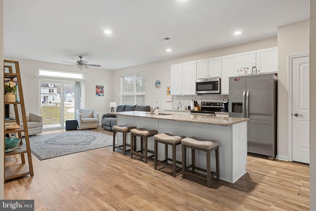 kitchen with a center island with sink, light stone counters, appliances with stainless steel finishes, white cabinets, and a breakfast bar area