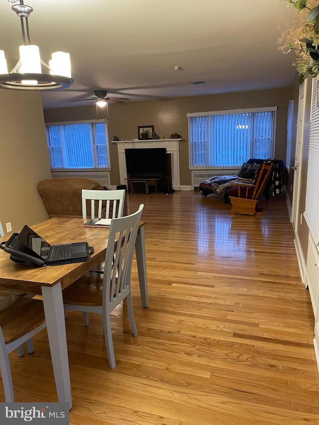 dining area featuring ceiling fan, a fireplace, and light hardwood / wood-style floors