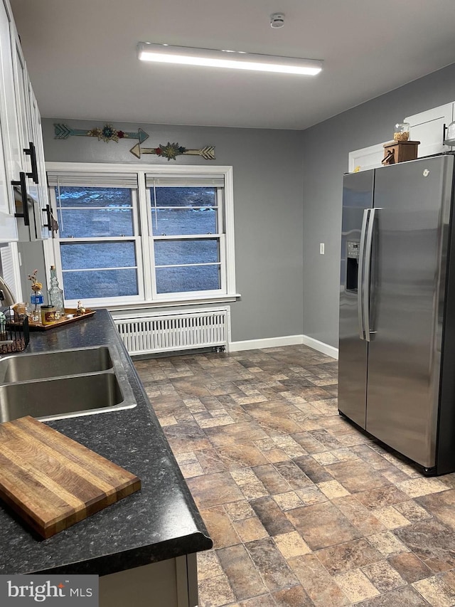 kitchen featuring radiator heating unit, stainless steel fridge, sink, and white cabinets