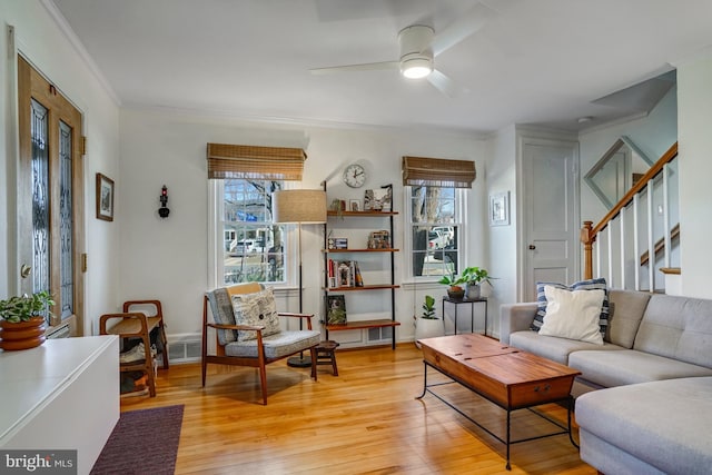 living room featuring light wood-style flooring, stairs, ornamental molding, and ceiling fan