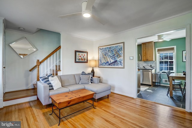 living room featuring light wood-type flooring, crown molding, stairway, and a ceiling fan