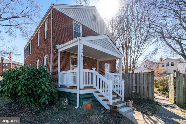 bungalow-style house featuring covered porch, brick siding, and fence