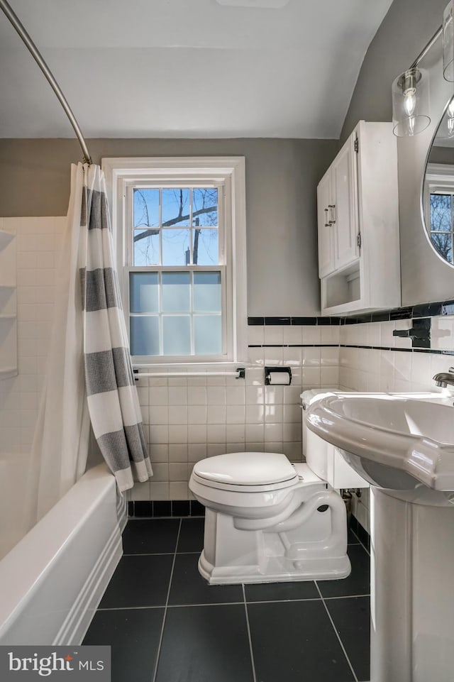 bathroom featuring tile walls, toilet, shower / bath combo with shower curtain, a sink, and tile patterned flooring