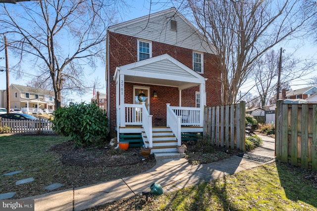 view of front of house with covered porch, brick siding, and fence