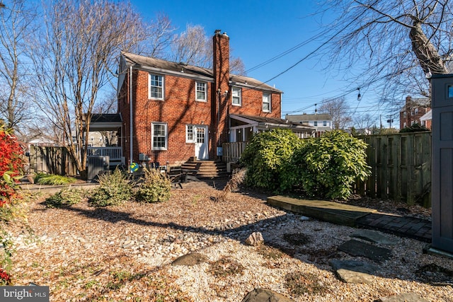 rear view of house featuring a chimney, fence, and brick siding