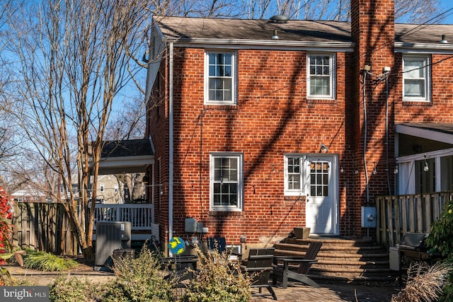 back of house with central AC, brick siding, a chimney, and fence