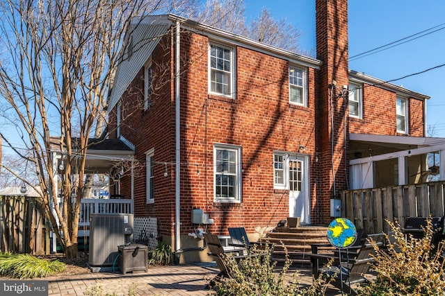 rear view of house featuring brick siding, a patio, a chimney, fence, and cooling unit