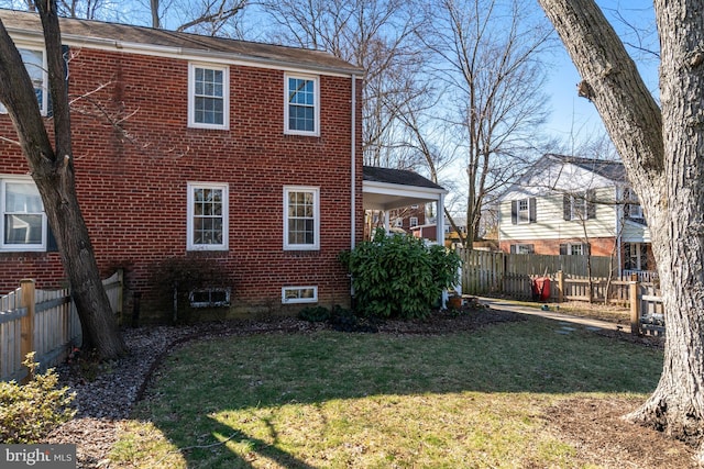 view of home's exterior with brick siding, a lawn, and fence