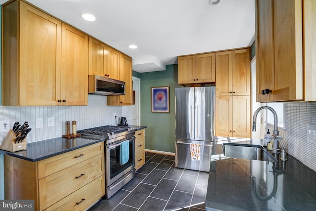 kitchen with tasteful backsplash, appliances with stainless steel finishes, a sink, dark tile patterned floors, and baseboards