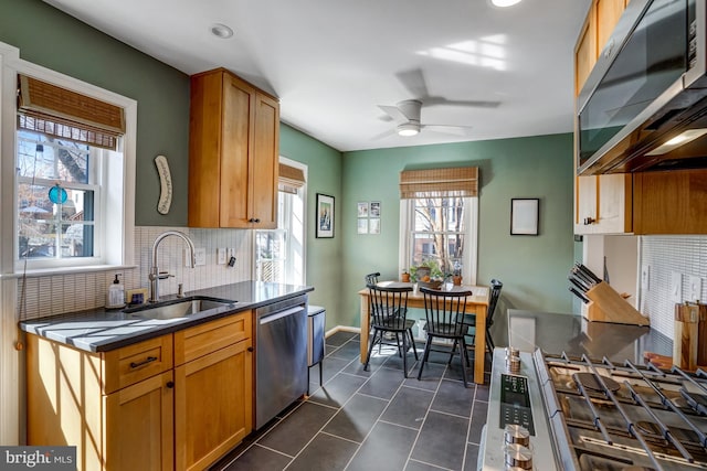 kitchen with stainless steel appliances, dark tile patterned flooring, a sink, tasteful backsplash, and dark countertops