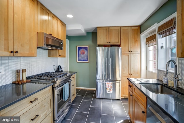 kitchen featuring tasteful backsplash, appliances with stainless steel finishes, a sink, dark stone countertops, and dark tile patterned floors