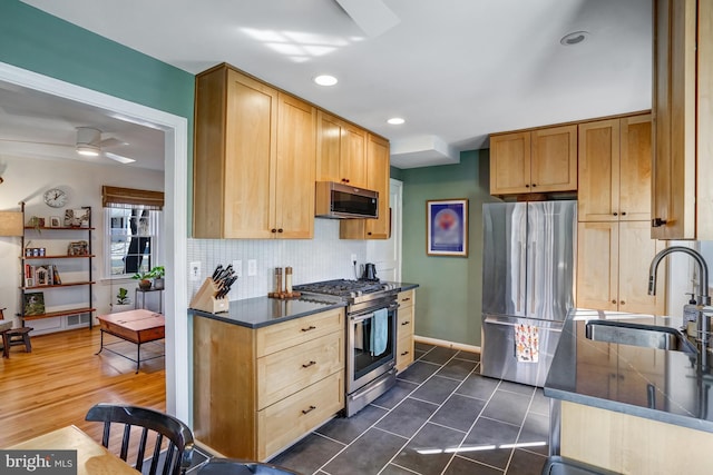 kitchen featuring ceiling fan, stainless steel appliances, a sink, backsplash, and dark countertops