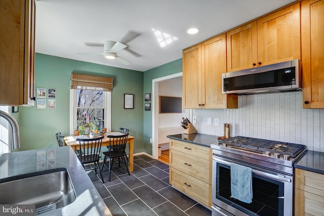 kitchen featuring dark countertops, ceiling fan, appliances with stainless steel finishes, a sink, and backsplash