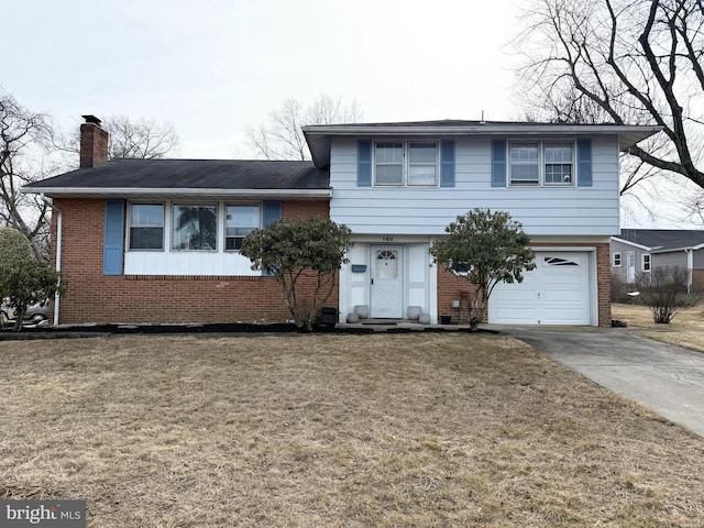 split level home with a garage, brick siding, a chimney, and a front yard