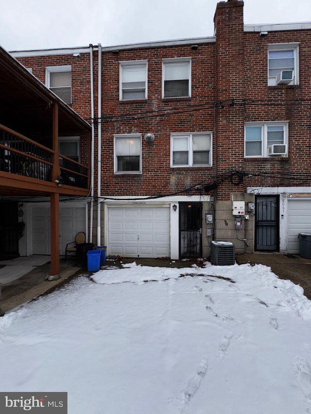 snow covered back of property with cooling unit and a garage