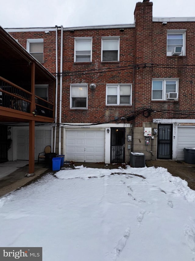 snow covered property with a garage and cooling unit