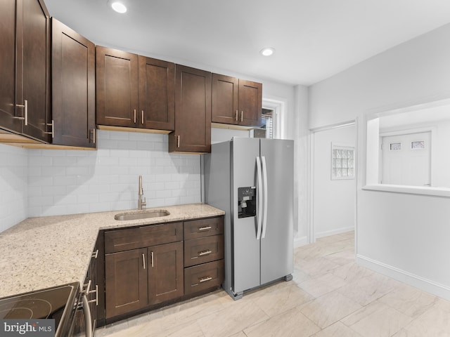 kitchen featuring dark brown cabinetry, stainless steel refrigerator with ice dispenser, sink, and light stone counters