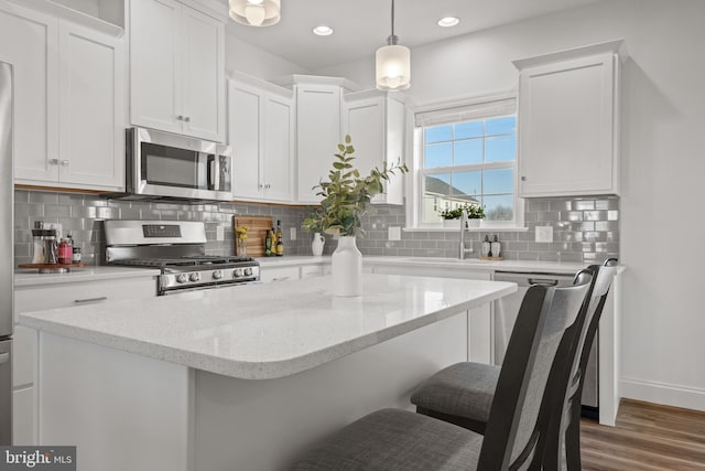 kitchen featuring a kitchen bar, sink, white cabinetry, decorative light fixtures, and stainless steel appliances